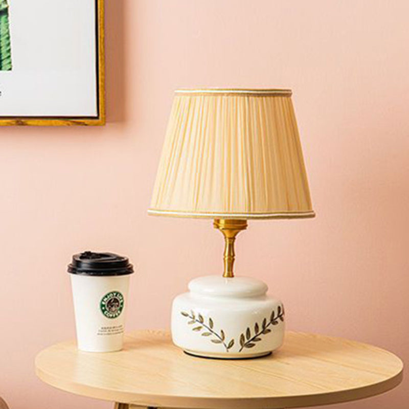 Lampe de table à 1 lumière avec abat-jour en tissu plissé trapézoïdal contemporain et base en céramique ronde pour chambre 