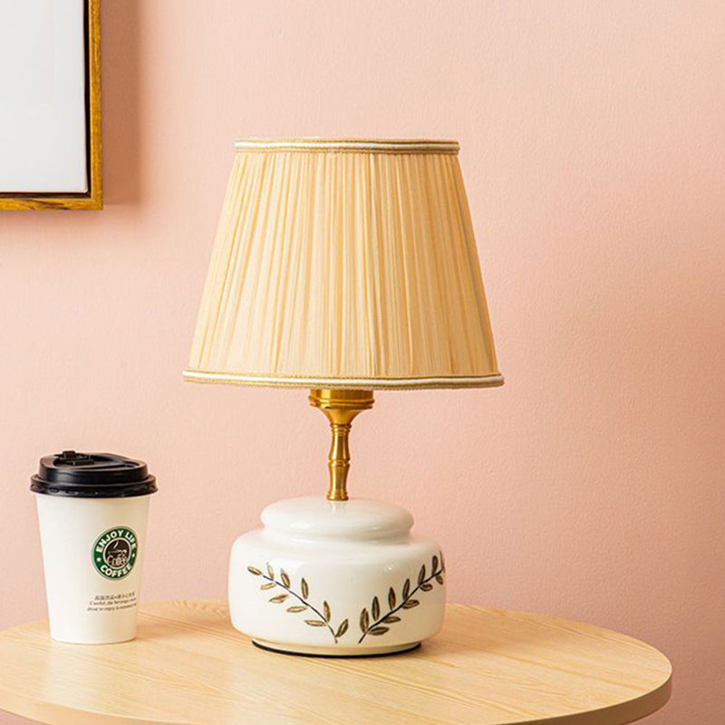 Lampe de table à 1 lumière avec abat-jour en tissu plissé trapézoïdal contemporain et base en céramique ronde pour chambre 