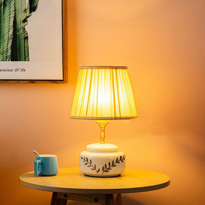 Lampe de table à 1 lumière avec abat-jour en tissu plissé trapézoïdal contemporain et base en céramique ronde pour chambre 